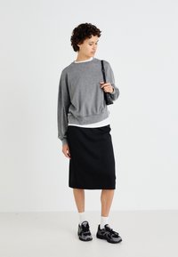 Sweatshirt cinza oversized com um acabamento texturizado, sobre um top branco, combinado com uma saia lápis preta e sapatilhas de desporto pretas.