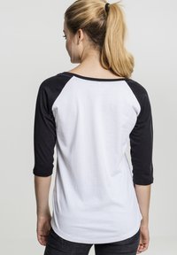 Zwart-wit baseballshirt met driekwartmouwen, met een witte romp en zwarte raglanmouwen. Geweven van een zachte katoenen stof, met een casual pasvorm.