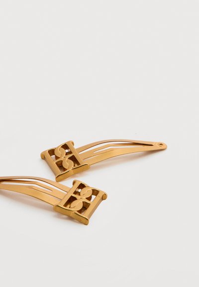 Δύο λεπτές χρυσές φουρκέτες με γεωμετρικό σχέδιο κοπής στη μία άκρη, τοποθετημένες σε λευκό φόντο.
