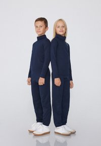 Navyblaue Rollkragenoberteile und passende Hosen aus glattem Stoff in lockerer Passform. Beide Kinder tragen weiße Sneakers.