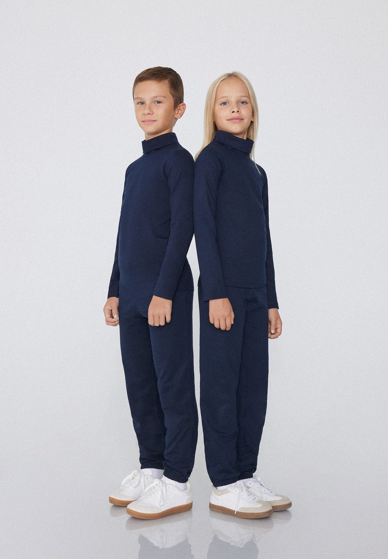 Navyblaue Rollkragenoberteile und passende Hosen aus glattem Stoff in lockerer Passform. Beide Kinder tragen weiße Sneakers.