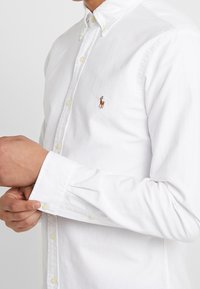 Witte katoenen blouse met knopen, voorzien van een klassieke kraag, lange mouwen en een klein geborduurd logo op de borst.