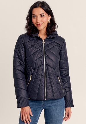 Veste rembourrée matelassée bleu marine avec capuche, dotée d'une fermeture éclair à l'avant, de deux poches latérales zippées et d'un motif de couture texturé sur les manches.