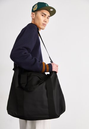 Black duffel bag with sturdy handles and adjustable shoulder strap, made of smooth, matte material. Features minimalistic design with no visible logos.