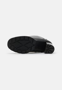 Suela de bota de cuero negro con goma texturizada, que presenta profundas estrías y un patrón circular para mayor tracción. Tacón redondeado para estabilidad.