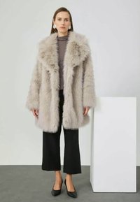 Faux fur coat in light gray, featuring a wide collar, long sleeves, and a loose silhouette, paired with a fitted top and cropped black pants.