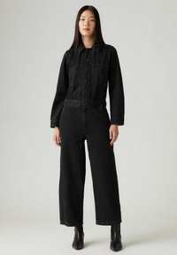 Czarny denimowy kombinezon z kołnierzykiem, długimi rękawami, przednimi kieszeniami i szerokimi nogawkami. Gładka tekstura i ciemny odcień z przeszyciami.