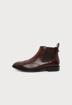 Brown leather Chelsea boot with elastic side panels, low heel, and pull tab at the back on white background.