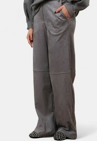 Pantaloni larghi grigi realizzati in un tessuto liscio, con tasche laterali e dettagli delle cuciture visibili. Abbinati a scarpe nere con borchie.