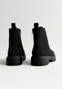 Bottines en suède noir avec une finition texturée, des panneaux latéraux élastiques et une semelle en caoutchouc épaisse présentant des motifs de sculpture visibles.