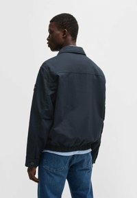 Giacca leggera blu navy con colletto, vita elasticizzata e polsini con bottone, caratterizzata da un piccolo logo sulla manica.