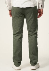Green cotton pants with a straight leg design, featuring a smooth texture and back pockets, paired with white sneakers.