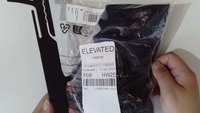 Hands holding a sealed package of black leggings labeled "ELEVATED Leggings" with size and SKU details visible on the label.