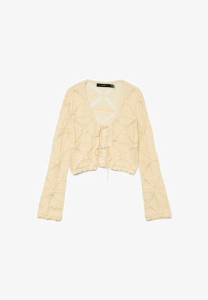 Kremast pulover iz kvačkanja z dolgimi rokavi, V-izrezom in zavezanjem spredaj. Ima teksturirane diamante in valovito obrobje. Lahka pletenina.