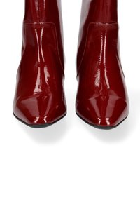 Stivaletti alla caviglia in pelle verniciata rossa con finitura lucida, punta affilata e texture liscia; presentano un design elegante senza hardware visibile.