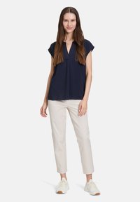 Marineblaue V-Ausschnitt-Bluse mit kurzen Ärmeln, fließendem Stoff, kombiniert mit cremefarbene, schmal zulaufende Hosen und weißen Sneakers, was ein lässiges Outfit ergibt.