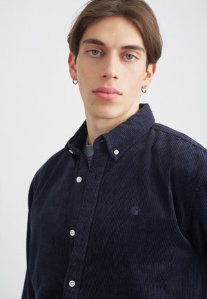 Tengerészkék bordázott ing, gombos gallérral, texturált anyaggal és hímzett logóval. Fehér gombokkal és lazább szabással rendelkezik.