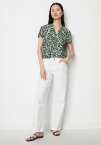 Kurzärmlige grüne Bluse mit schwarzem Punktmuster, kombiniert mit weißen geraden Jeans und schwarzen flachen Sandalen. Einfaches Design, lockere Passform.