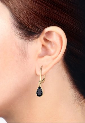 Boucle d'oreille créole en ton or avec une pierre précieuse noire en forme de goutte taillée suspendue à un fermoir sécurisé, mettant en valeur des lignes épurées et un design élégant.