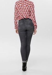 Jeans in denim scuro slim-fit, con due tasche posteriori, abbinati a una blusa a maniche lunghe con motivo rosso e bianco e tacchi neri.