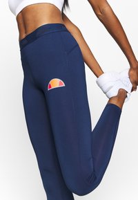 Leggings blu navy realizzati in materiale elasticizzato, con un logo colorato sul lato. La texture liscia e il design aderente migliorano la mobilità.