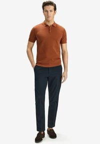 Kortärmad polo i texturerad rödbrun tyg, kombinerad med marinblå byxor och bruna loafers. Har en krage och treknapps placket.
