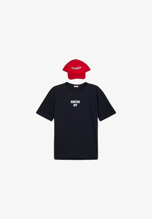 Camiseta navy con el texto "ROUTINE OFF" en blanco; acompañada de una gorra roja con un motivo de hoja blanca. Ambos artículos son informales y ajustados.