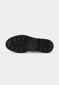 Semelle de botte en caoutchouc noir avec des rainures profondes et des motifs en forme de croix pour une meilleure traction, présentée sur un fond uni.