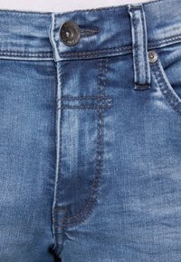 Hellblaues Denim-Jeans mit klassischem Fünf-Taschen-Design, metallischem Knopfverschluss und gesteppten Akzenten sowie einer verwaschenen Textur.