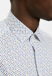 Weißes Hemd mit kleinem, mehrfarbigem Blattmuster in Blau, Lila und Beige. Verfügt über einen klassischen Kragen und eine glatte Textur.