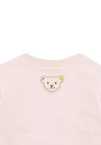Pink cotton shirt with a round neckline featuring an embroidered bear face patch; texture is soft; minimalistic design and detailing.