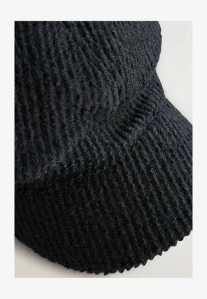 Primo piano di una sciarpa in lana nera lavorata a maglia, piegata, con una texture a costine su uno sfondo chiaro.