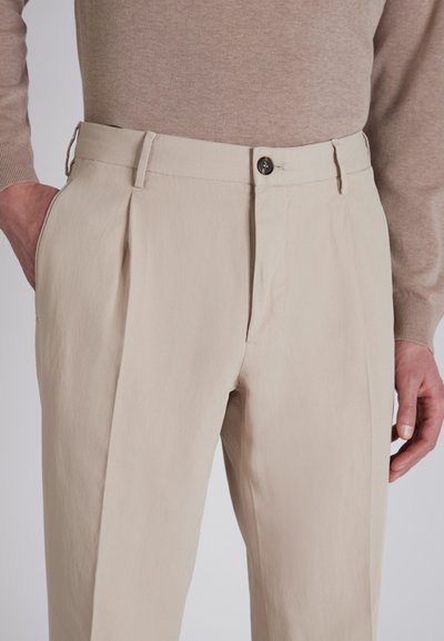 Beżowe spodnie plisowane wykonane z teksturowanej tkaniny, z zapięciem na guzik z przodu i kieszeniami bocznymi, w luźnym kroju.