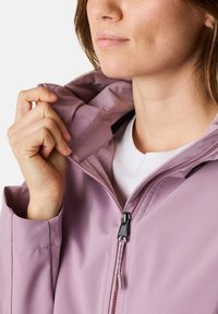 Lila Softshell-Jacke mit durchgehendem Reißverschluss, verstellbarem Kragen und glatter Textur. Verfügt über einen schwarzen Reißverschluss mit passendem Zipper.