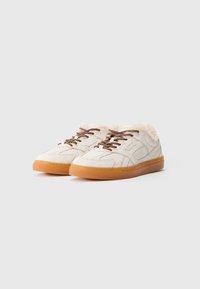 Zapatillas de ante de color blanco roto con cordones marrones, suelas de goma y un forro de color crema visible en el cuello.