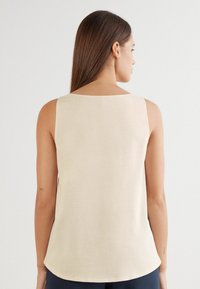 Beiges ärmelloses Oberteil mit quadratischem Rückendesign, glatter Textur und leicht gewelltem Saum. Minimalistischer Stil ohne sichtbare Beschläge oder Muster.