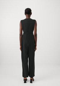 Salopette nera senza maniche con vita cintata, design a gamba larga e due tasche posteriori. Tessuto dal tocco liscio, stile minimalista.