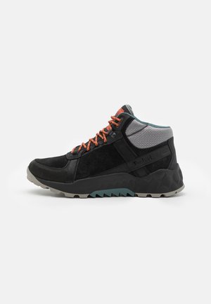 Bota de senderismo negra y gris con cordones naranjas, cuello acolchado en el tobillo, suela texturizada y logotipo lateral.