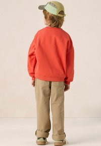 Sweat-shirt orange, pantalon beige retroussé, casquette verte et beige, et chaussures beige. Une tenue décontractée composée de matériaux doux et confortables.