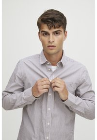 Camicia a righe con sottili motivi bianchi e marroni, chiusura con bottoni sul davanti, maniche lunghe, tessuto morbido e un piccolo taschino sul petto.
