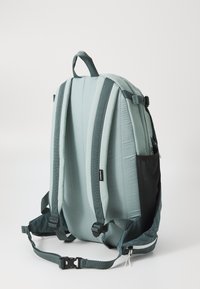 Ryggsäck med en mjuk, vadderad mintgrön utsida, mörkgröna remmar, en sidoficka och en smidig, minimalistisk design. Har justerbara remmar.