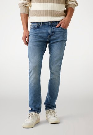 Slank fitte lichtblauwe spijkerbroek met vervaagde textuur, klassiek vijf-pocket ontwerp en een knoopsluiting, gecombineerd met witte sneakers.