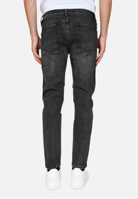 Jeans in denim nero slim fit con una texture sbiadita, stile a cinque tasche e dettagli di cucitura visibili, abbinati a sneaker bianche.