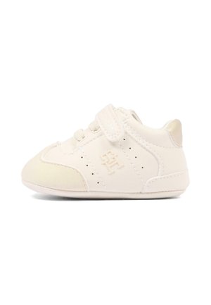 Petite basket blanche pour bébé avec une bride Velcro, une semelle souple et un logo brodé sur le côté sur fond blanc.