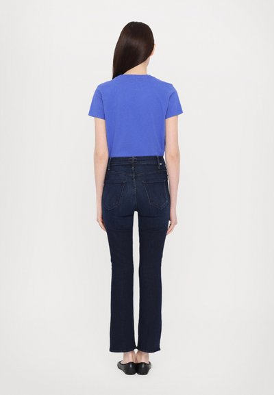 Blå t-skjorte med korte ermer kombinert med mørke denim flare bukser, som viser en tettsittende silhuett og en jevn tekstur. Enkel design uten mønster.