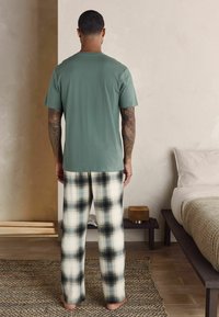T-shirt en coton vert et pantalon de pyjama en plaid dans des tons crème, noir et vert. Les pantalons ont une coupe décontractée et une texture douce.