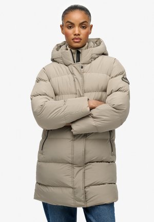 Beige gewatteerde jas met een capuchon, voorzien van horizontale stiksels, zijritsen en een logo-accent op de mouw. Warme en functionele ontwerp.