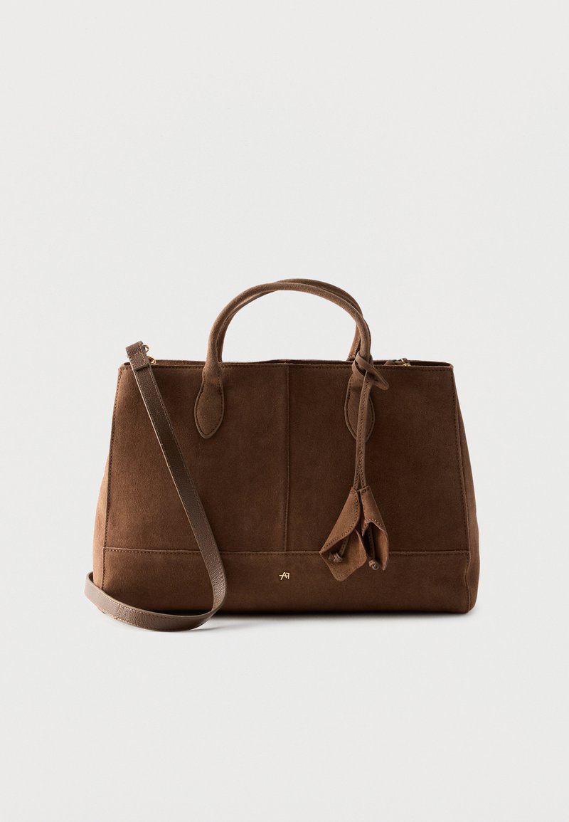 Καφέ τσάντα σουέτ με δύο χερούλια, αποσπώμενο λουρί ώμου και διακοσμητικά σουέτ φούντες, που παρουσιάζεται σε απλό φόντο.