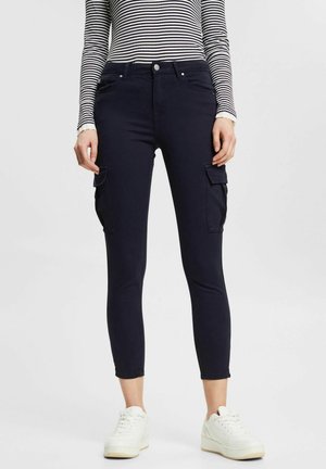 Pantalones cargo azul marino con un diseño ajustado, que presentan dos bolsillos laterales y una textura suave. Combinados con una camiseta de rayas de manga larga y zapatillas blancas.