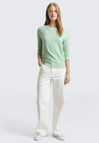 Lichtgroene, gestructureerde top met lange mouwen, gecombineerd met witte broek met wijde pijpen en witte sneakers, voorzien van een ronde halslijn en aangesloten manchetten.